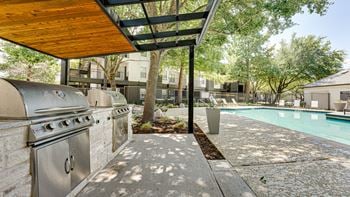 A stainless steel bbq grill is on a patio next to a pool.